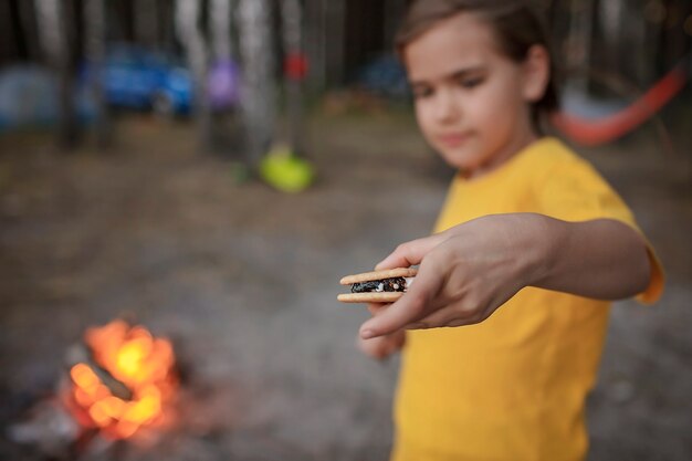 Girl roasting marshmallow to make smores over fire flame during camping traditional travel food