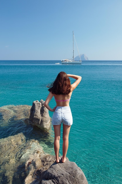 Girl on the rock looking to the yacht on sea