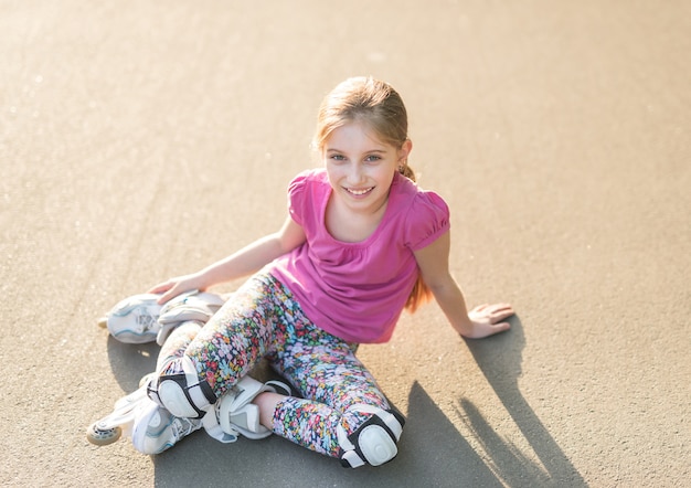 Girl rollerblading sitting on asphalt, stretching