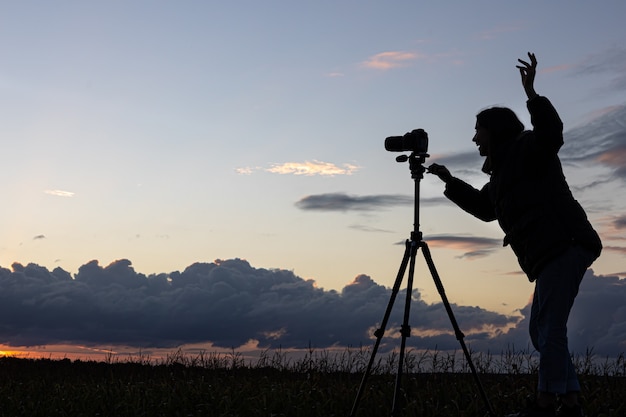 La ragazza sul tetto dell'auto fotografa il tramonto con un treppiede.