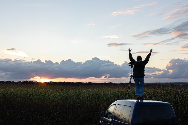 車の屋根の上の女の子は、三脚で夕日を撮影します。