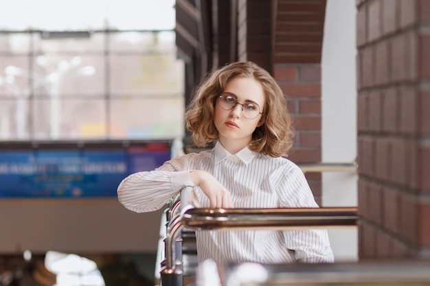 girl in round transparent glasses looks at the camera. curly hair. hipster background blurred concept.walk around the mall