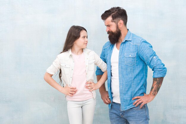 Girl rules Naughty girl being nasty Small girl child with father on grey background Adorable little girl and bearded man putting hands on hips