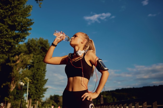 Il corridore della ragazza beve l'acqua da una bottiglia nel parco.