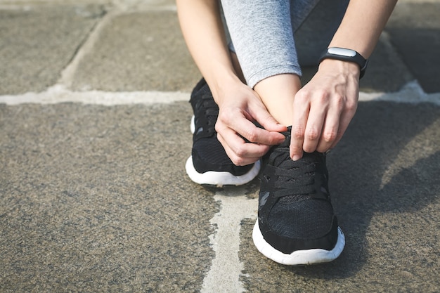 girl runner tying laces for jogging her shoes on road in a park