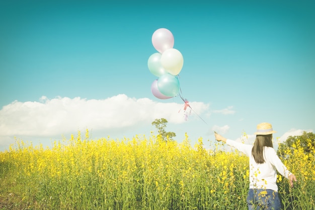 Girl running on the field of yellow flowerwith balloons at sunset. Happy woman on nature, concept about carefree airiness and relax, vintage effect