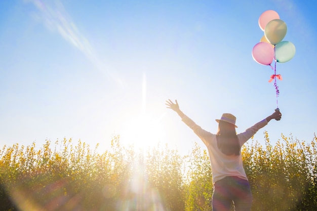 Girl running on the field of yellow flowerwith balloons at sunset. Happy woman on nature, concept about carefree airiness and relax, vintage effect