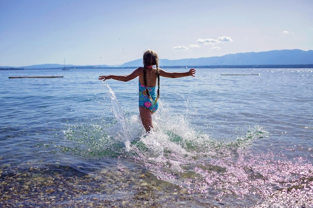 女の子は海に出くわし、太陽の光の中で水しぶき楽しい幸せ夏休みと旅行