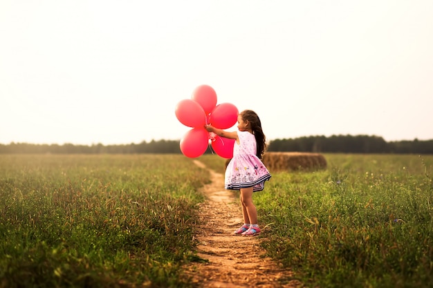 девушка бежит с красными воздушными шарами летом на природе