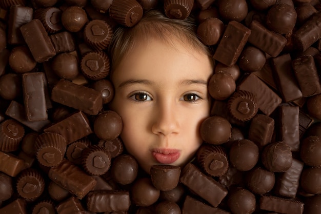 Girl's gezicht op een achtergrond van chocolade. overmatige consumptie van snoep is schadelijk voor de gezondheid