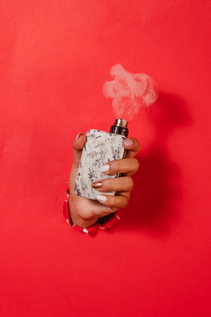 Girl's hand ataching a working vape machine, on a red background.