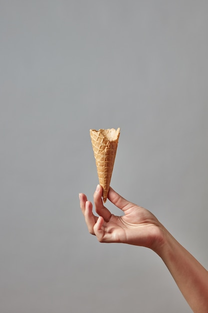 A girl's hand holds an empty crispy waffle cone on a gray wall.