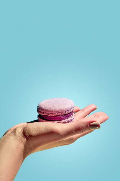 A girl's hand holds a pink macaron on a blue background French pastries