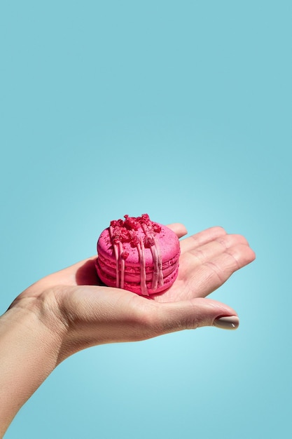 A girl's hand holds a pink macaron on a blue background French pastries