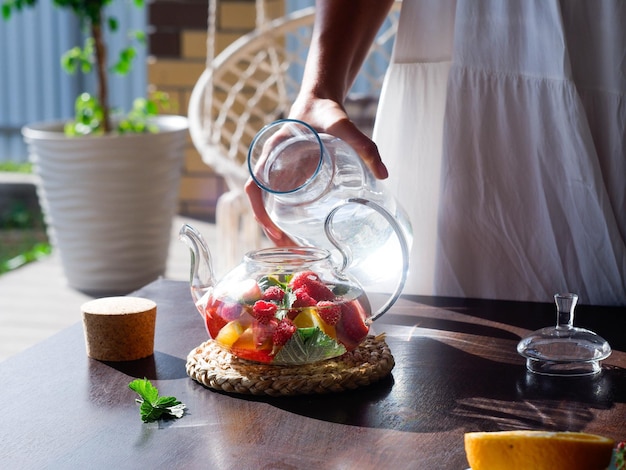 女の子の手が外のティーポットに水を注ぐ 夏の飲み物