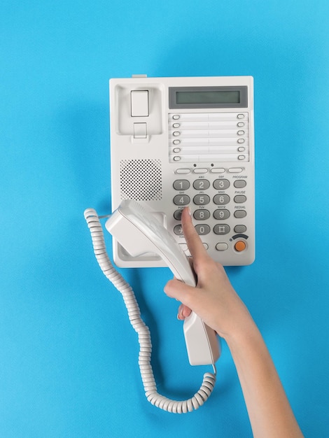 A girl\'s hand with a handset dials a number on a wired\
phone