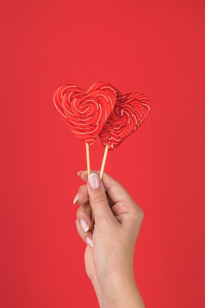 Рука девушки с двумя красными конфетами на красном фоне