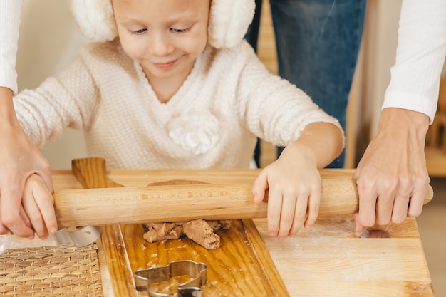 Girl's handen rollen gemberdeeg uit met een deegroller in de keuken Meisje bereidt kerstkoekjes op een houten tafel