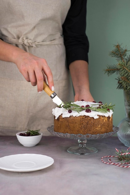 The girl's hands are cutting the Christmas cake with red berries on a gray table