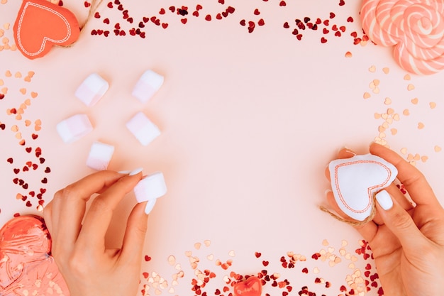 The girl's hands are holding a white heart and marshmallows on trendy pink paper. Valentine's day and womens day concept. Flat lay