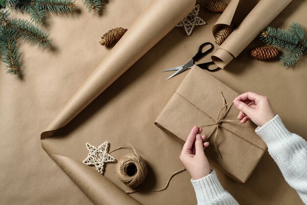 The girl's hands are tying a bow made of twine on a gift wrapped in craft paper. Christmas gift wrapping.