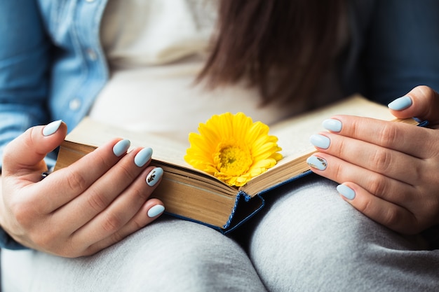 Foto mani della ragazza su un libro con un fiore giallo