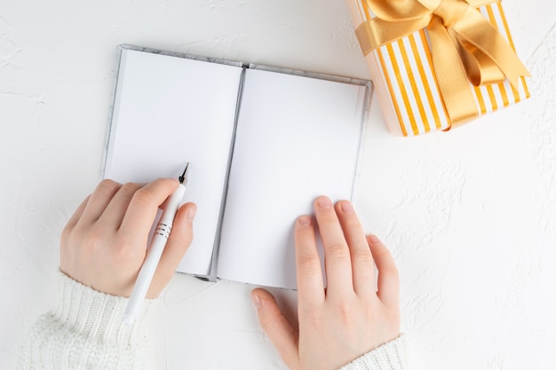 Girl's hands hold an blank notebook among gift box. Goals plans dreams make to do list 