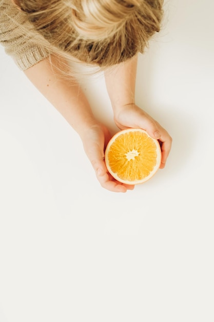 Photo girl's hands holding half of cutted orange on white background top view flat lay