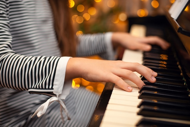 Girl's hands on the piano, close-up, beautiful bokeh in the background, woman playing the piano. Christmas lights and music, concert, family time, holidays concept.