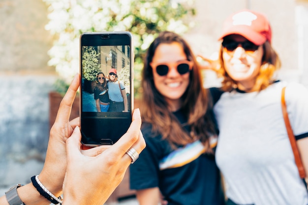 Girl's hands taking photo with a smartphone of a happy women lesbian couple in Madrid. 