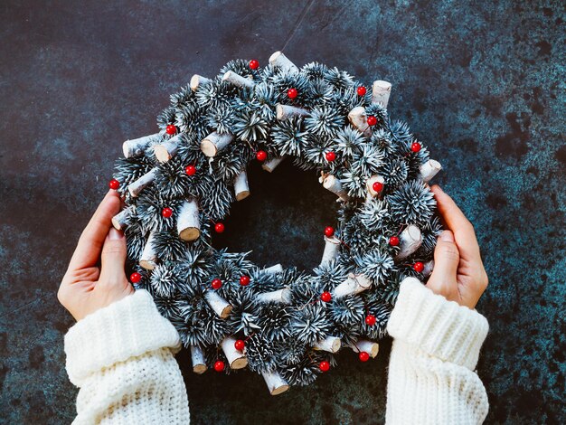 冬の白いセーターの女の子の手は青いテーブルにクリスマスの休日の花輪を保持します