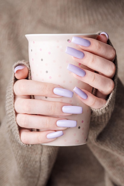 Girl's hands with delicate purple manicure holding a cup of tea