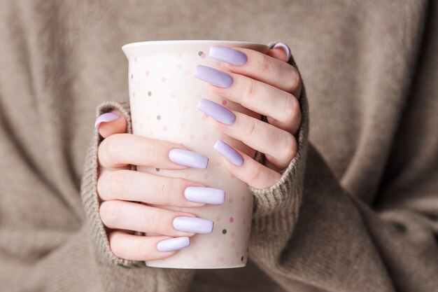 Girl's hands with delicate purple manicure holding a cup of tea