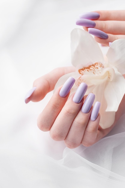 Photo girl's hands with delicate purple manicure and orchid flowers