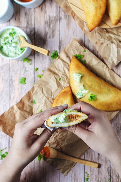 Girl's hands with empanada typical food from Venezuela adding gasacaca sauce, trio sauce, woodwn table