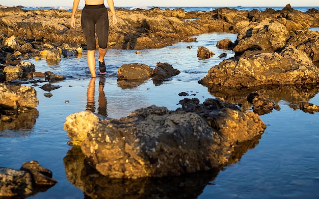 Girl's legs walking on the beach between stones In the background waves breaking on the rocks