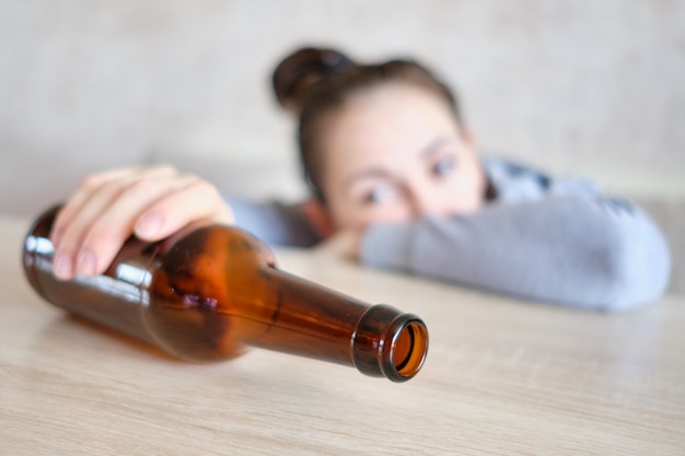 Foto la ragazza guarda tristemente la bottiglia di alcol.