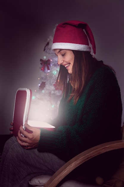 Girl in a Santa Claus hat, opens a box with a christmas present