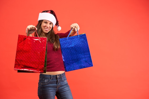 Girl in Santa Claus hat smiling with Christmas shopping bags on orange background.