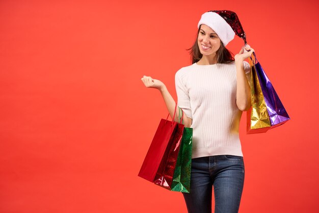 Girl in santa claus hat with christmas shopping bags on orange background