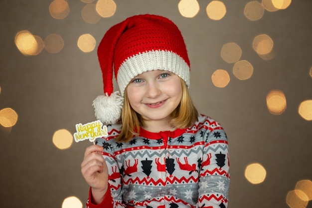 A girl in a santa hat holds a happy new year sign on a new year bokeh background