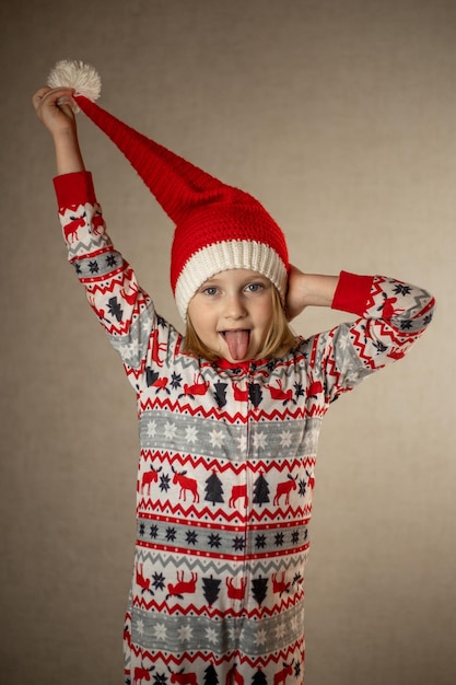 Girl in santa hat and New Year's pajamas on a solid background