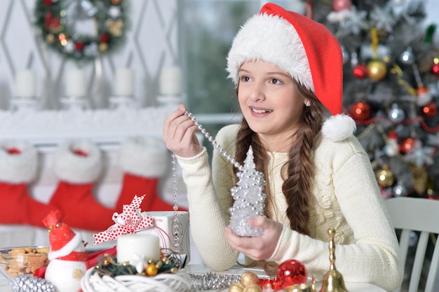 Girl in Santa hat preparing for Christmas sitting at the table