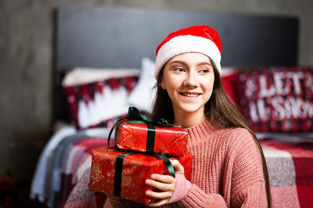 A girl in a Santa hat with gifts on the background of the New Year's interior.