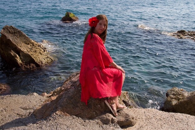 Foto una ragazza in un vestito scarlatto in riva al mare. vento, onde, spiaggia deserta. una vacanza al sud