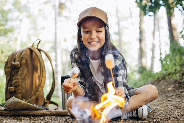 Photo girl scout frying marshmallows on fire at the woods