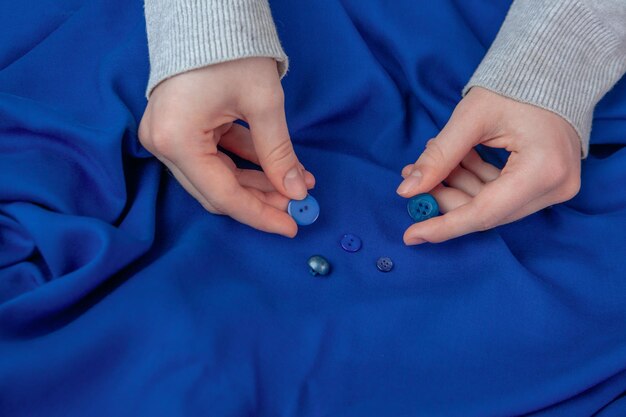 The girl selects buttons matching the color of the blue fabric Hobby sewing