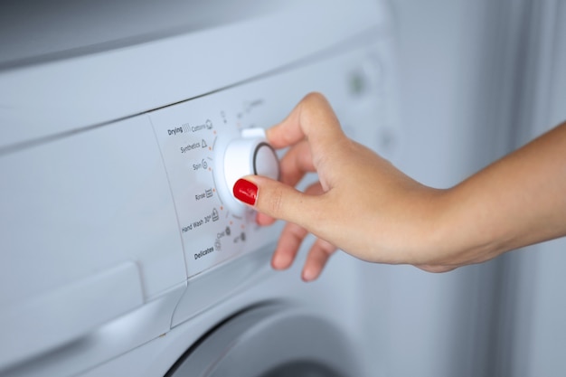 The girl sets the washing program for the washing machine.