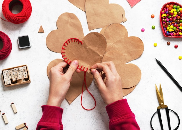 Girl sews the two pieces of the heart with a needle and red thread