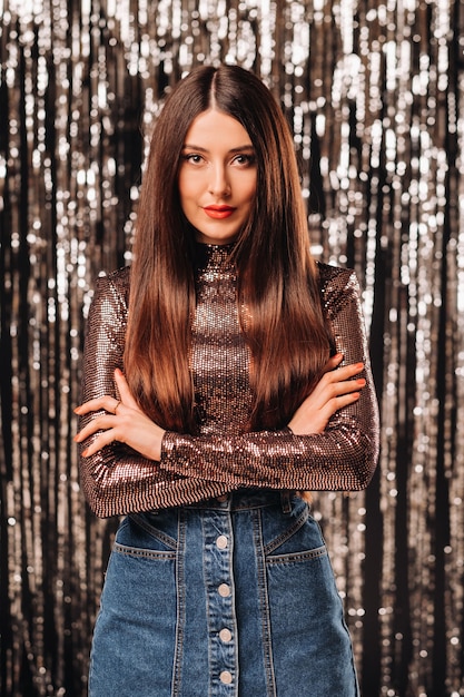 A girl in a shiny jacket on a silver background of New Year's rain.